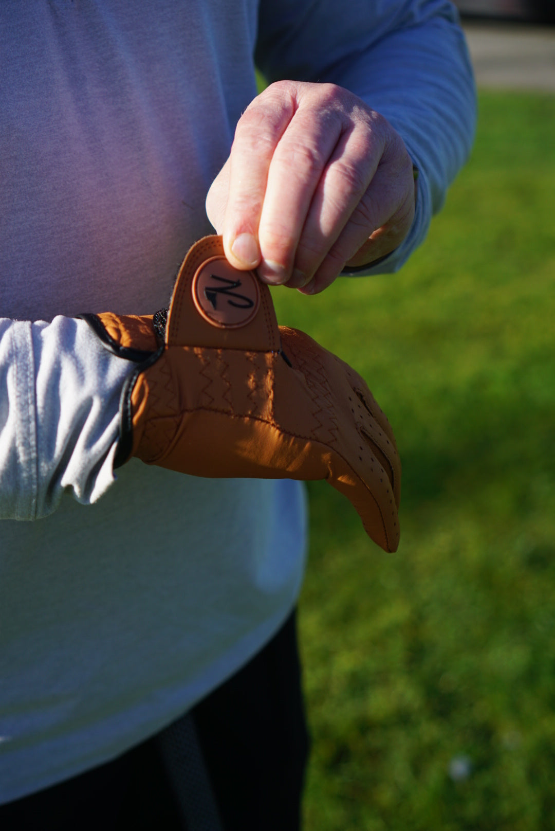 Close-up of a person wearing a brown Nova golf glove with a brand logo on a grassy background