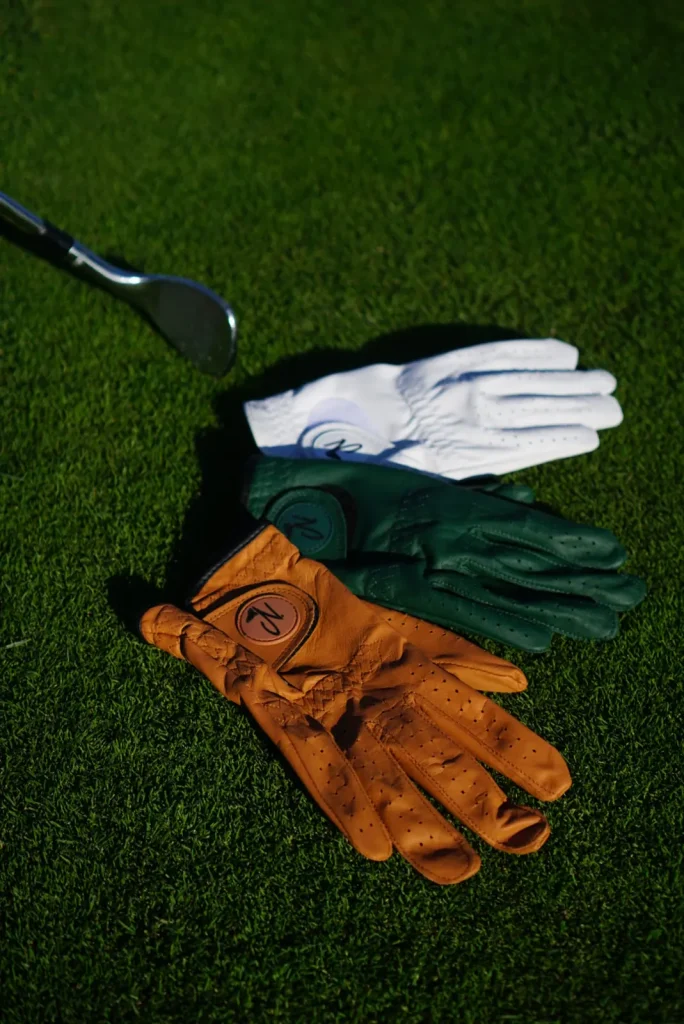 Three Nova golf gloves on the grass beside a club